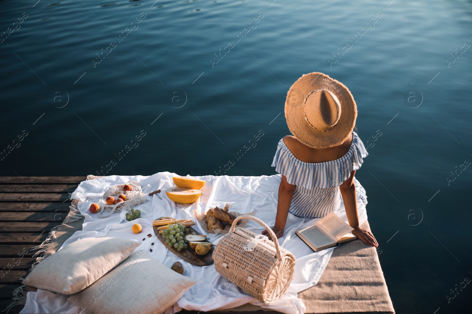 Photo of Young woman spending time on pier at picnic, back view