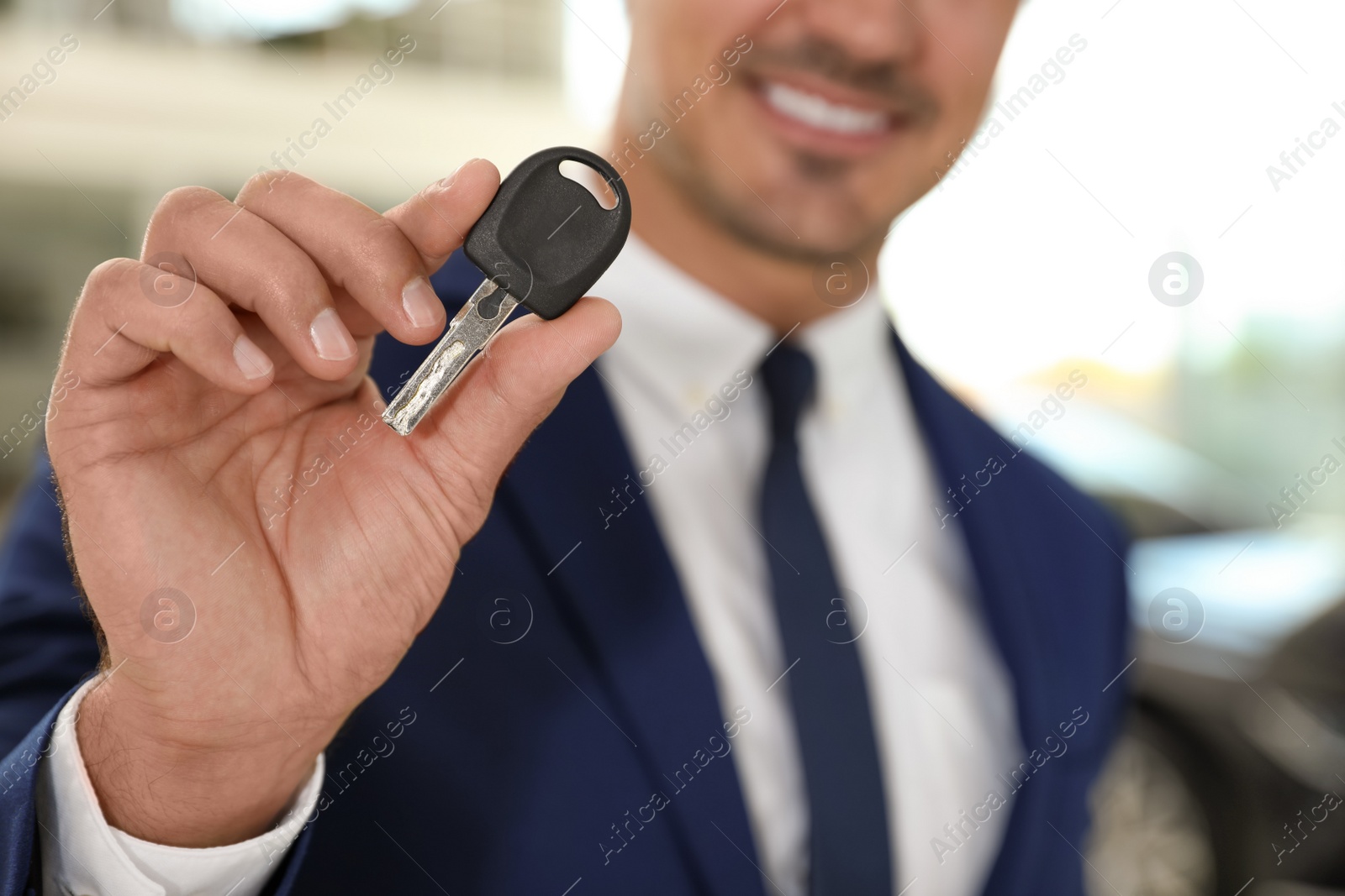 Photo of Young salesman with car key in modern dealership, focus on hand