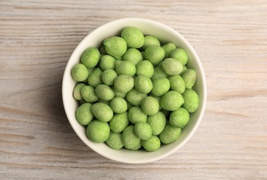 Photo of Tasty wasabi coated peanuts in bowl on white wooden table, top view