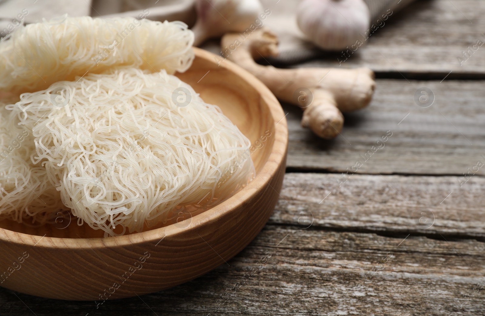 Photo of Bowl with dried rice noodles on wooden table, closeup. Space for text