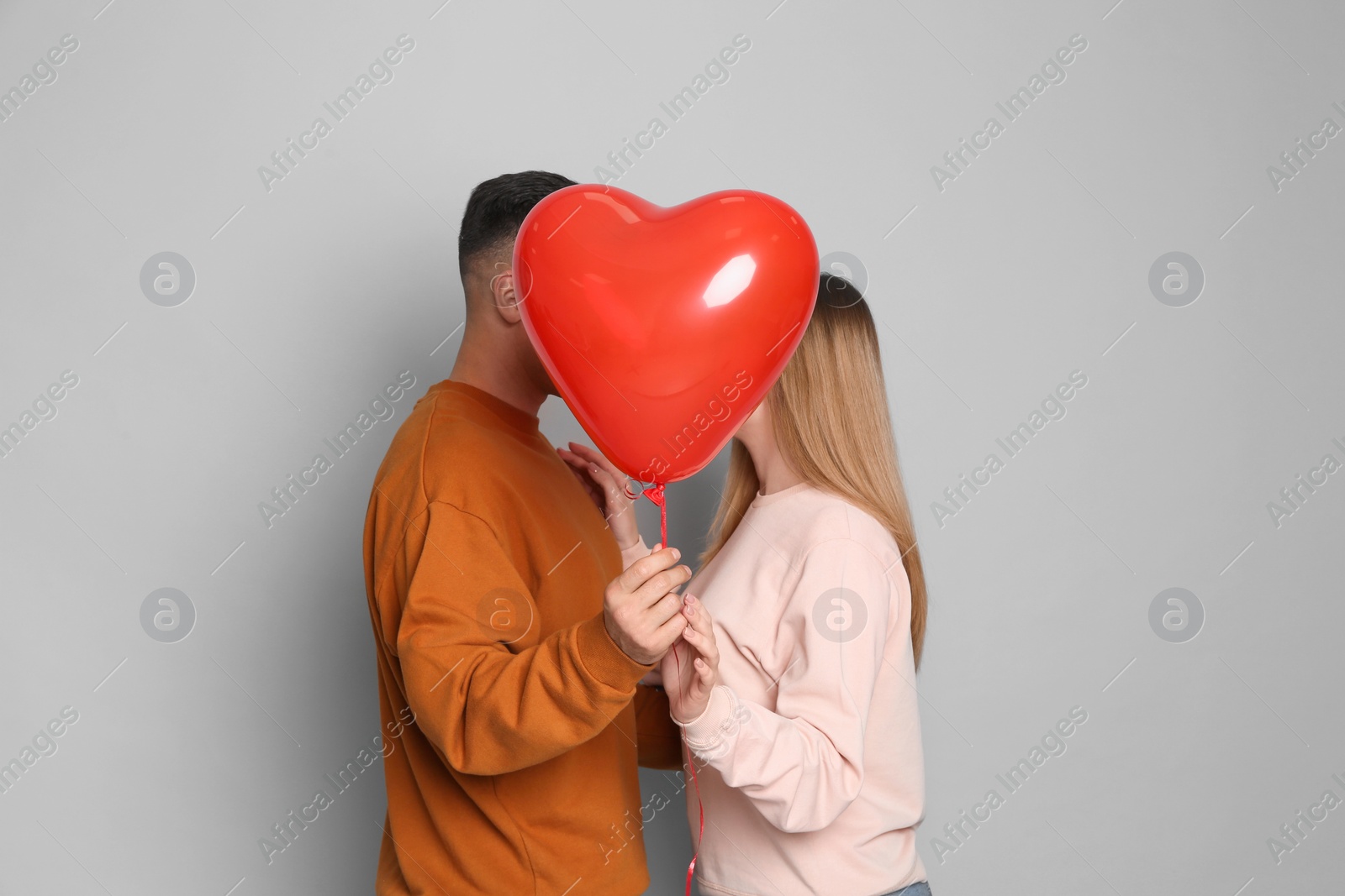 Photo of Lovely couple kissing behind heart shaped balloon on grey background. Valentine's day celebration