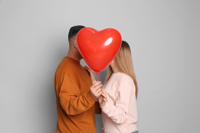 Lovely couple kissing behind heart shaped balloon on grey background. Valentine's day celebration