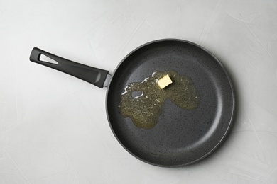 Frying pan with melting butter on grey table, top view