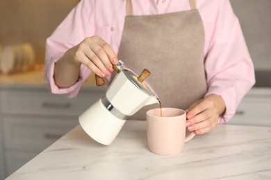 Woman pouring aromatic coffee from moka pot into cup at white marble table, closeup