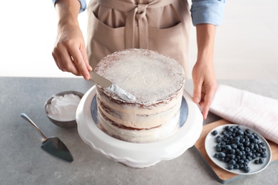 Woman decorating delicious cake with fresh cream on stand. Homemade pastry