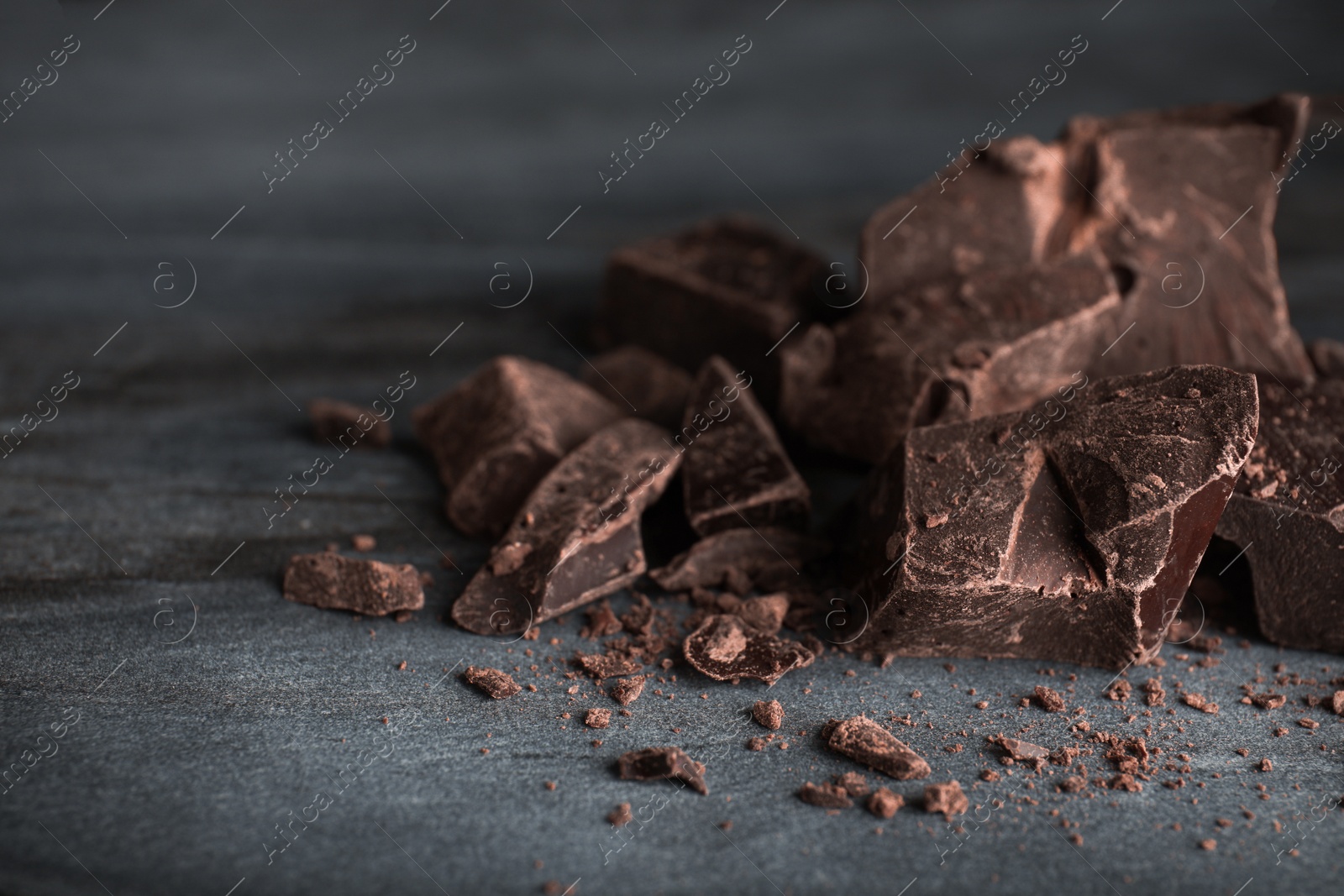 Photo of Pieces of dark chocolate on blue marble table, closeup