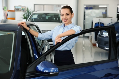 Photo of Young saleswoman near automobile in car dealership