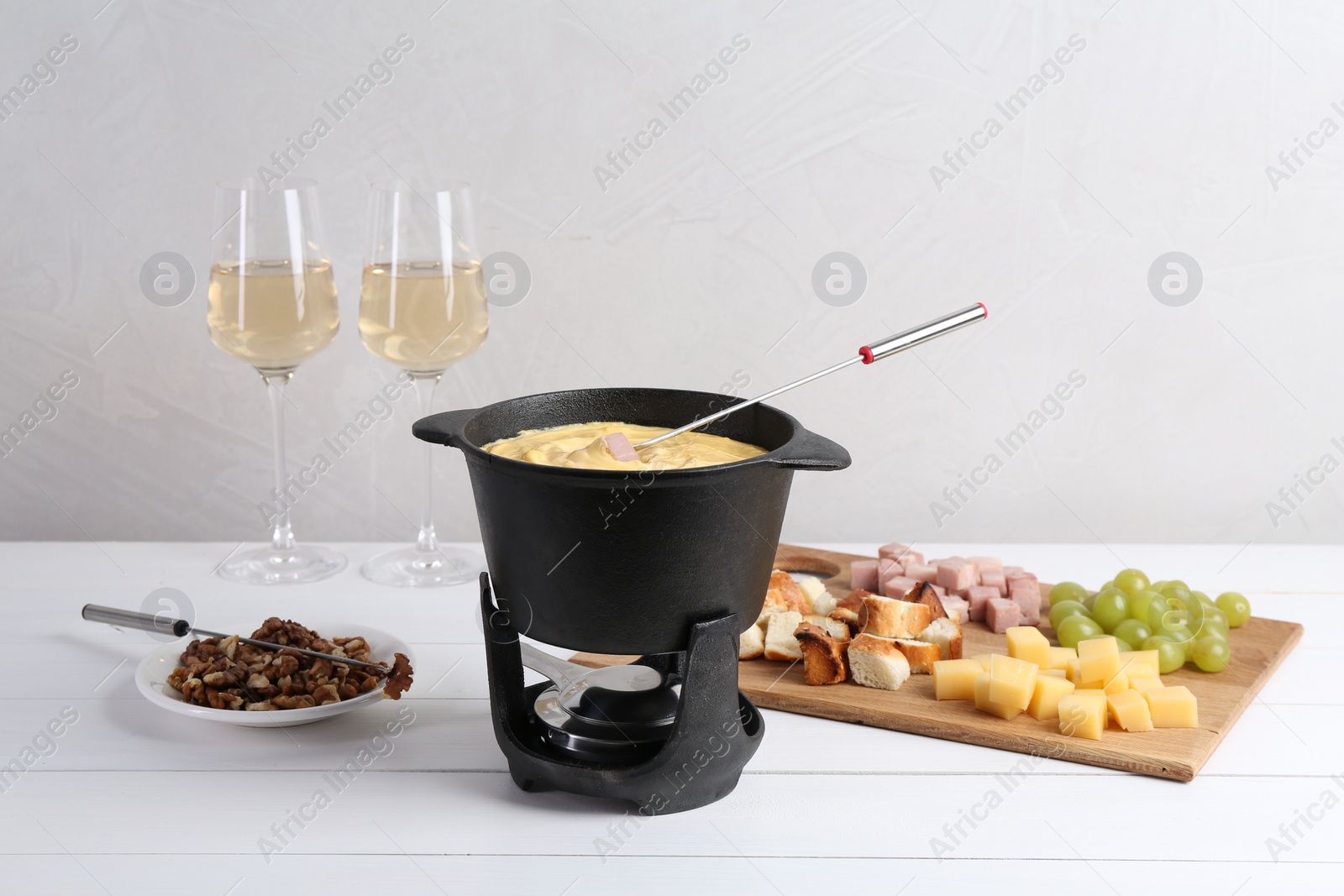 Photo of Fondue pot with tasty melted cheese, forks, wine and different snacks on white wooden table