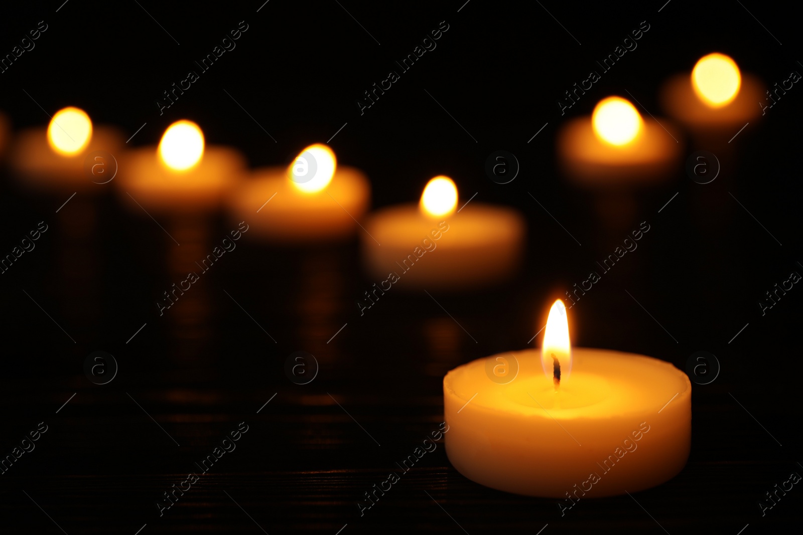 Photo of Burning candle on black table against blurred background, space for text