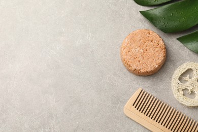 Photo of Solid shampoo bar, monstera leaf, comb and loofah on grey table, flat lay. Space for text