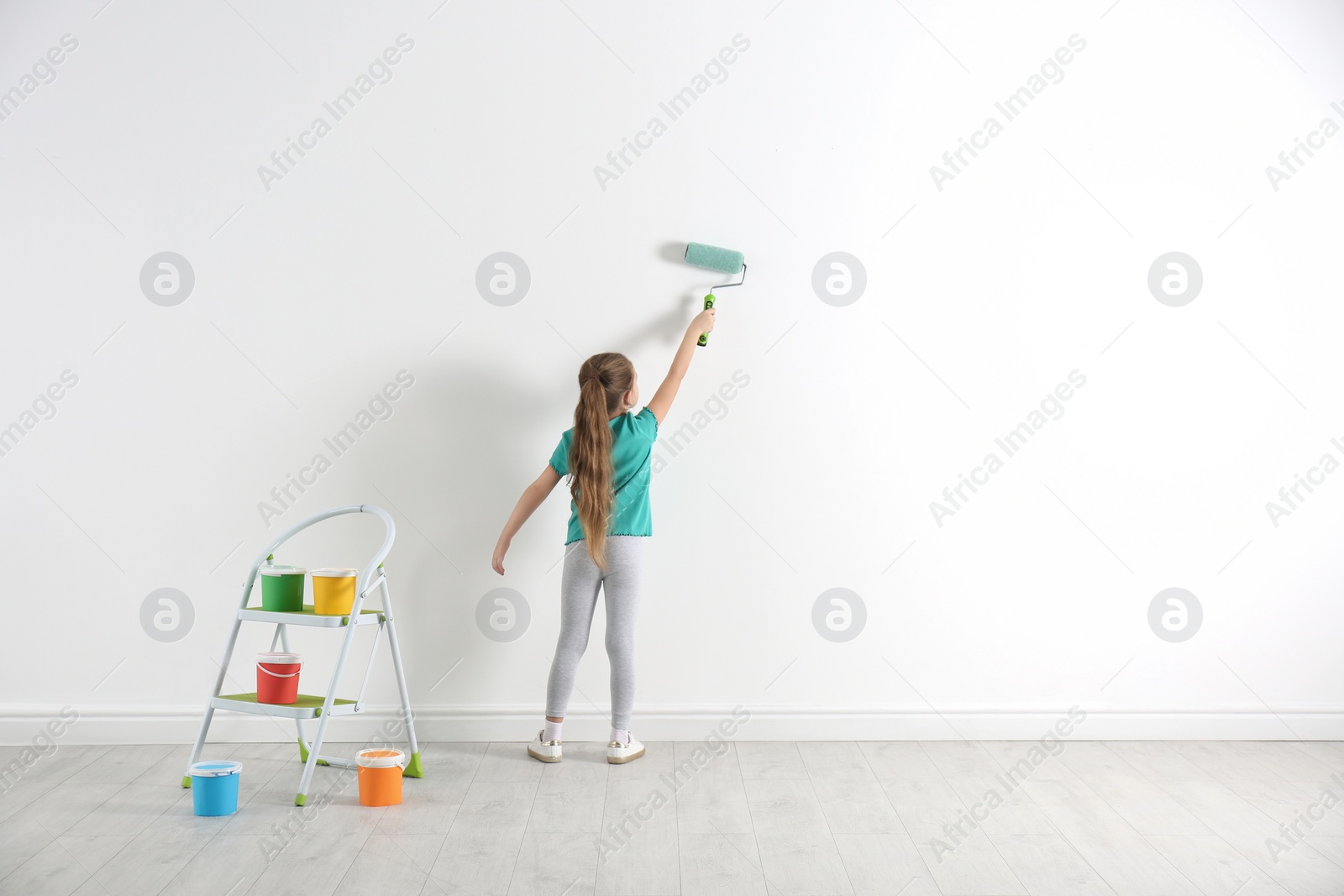 Photo of Little child painting with roller brush on white wall indoors. Space for text