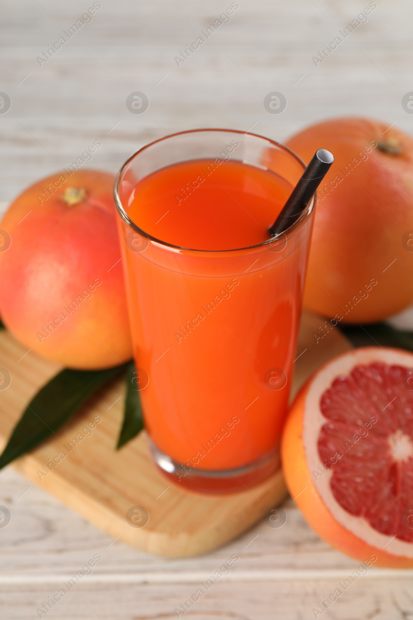 Photo of Tasty grapefruit juice in glass and fresh fruits on light wooden table, closeup