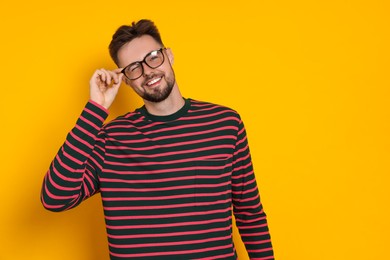 Photo of Handsome man in striped sweatshirt and eyeglasses on yellow background, space for text
