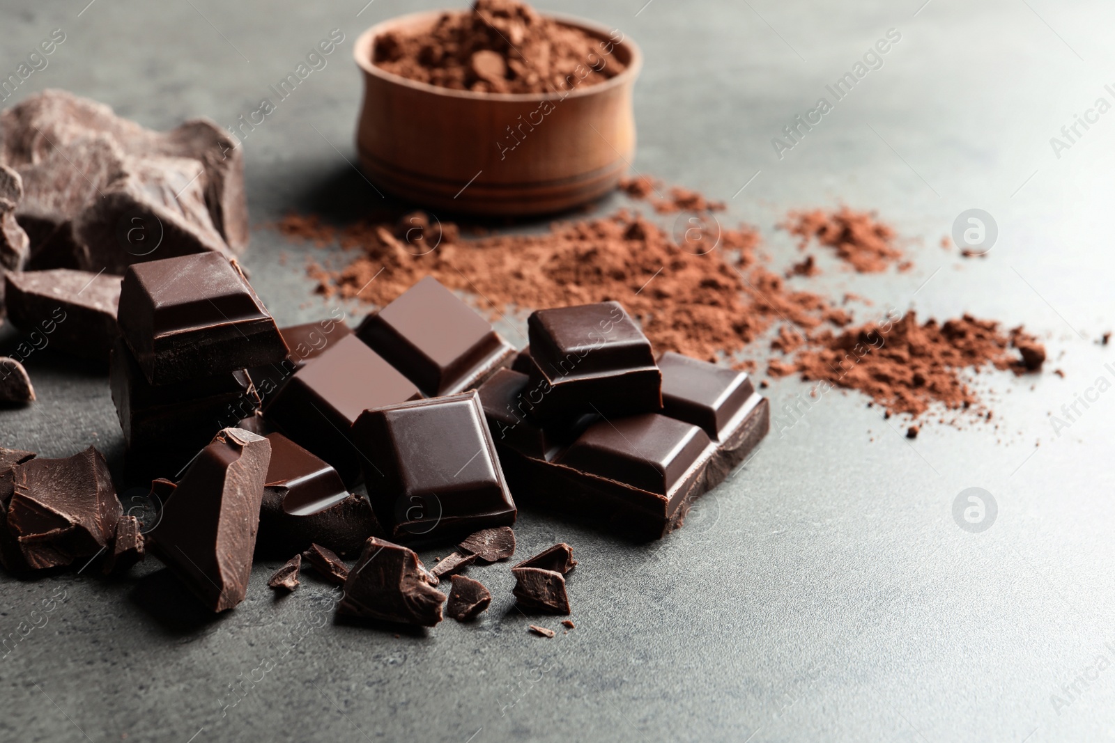 Photo of Pieces of chocolate and cocoa powder on grey background