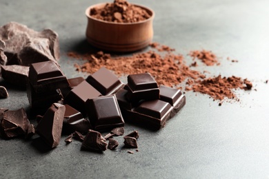 Pieces of chocolate and cocoa powder on grey background