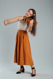 Beautiful woman playing violin on grey background