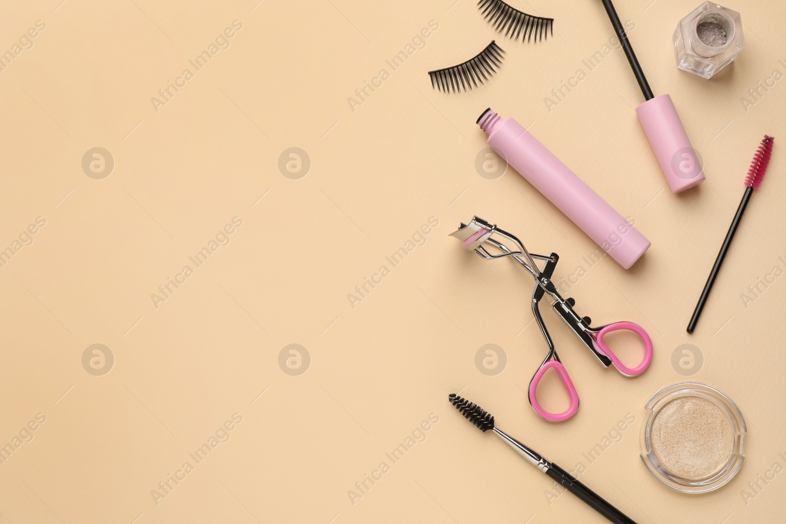 Photo of Flat lay composition with eyelash curler, makeup products and accessories on beige background. Space for text