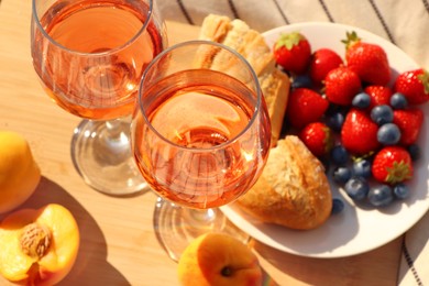 Photo of Glasses of delicious rose wine and food on wooden board, closeup