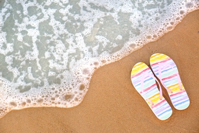 Photo of Stylish flip flops on sand near sea, top view with space for text. Beach accessories