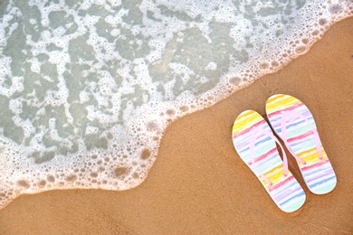 Stylish flip flops on sand near sea, top view with space for text. Beach accessories