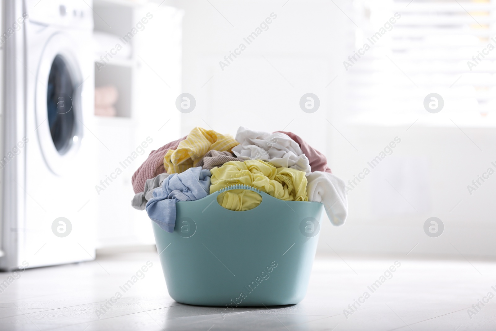 Photo of Light blue basket with dirty laundry on floor indoors