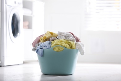 Photo of Light blue basket with dirty laundry on floor indoors