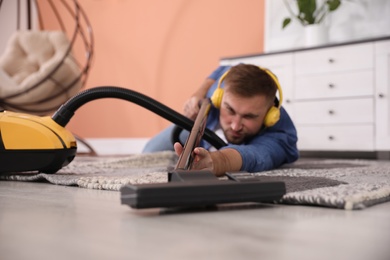 Photo of Young man having fun while vacuuming at home, focus on hand