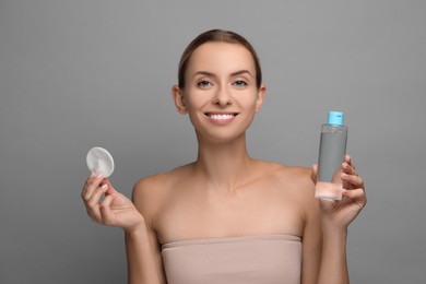Removing makeup. Smiling woman with cotton pad and bottle on grey background