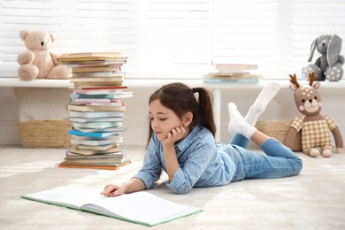 Photo of Little girl reading book on floor at home