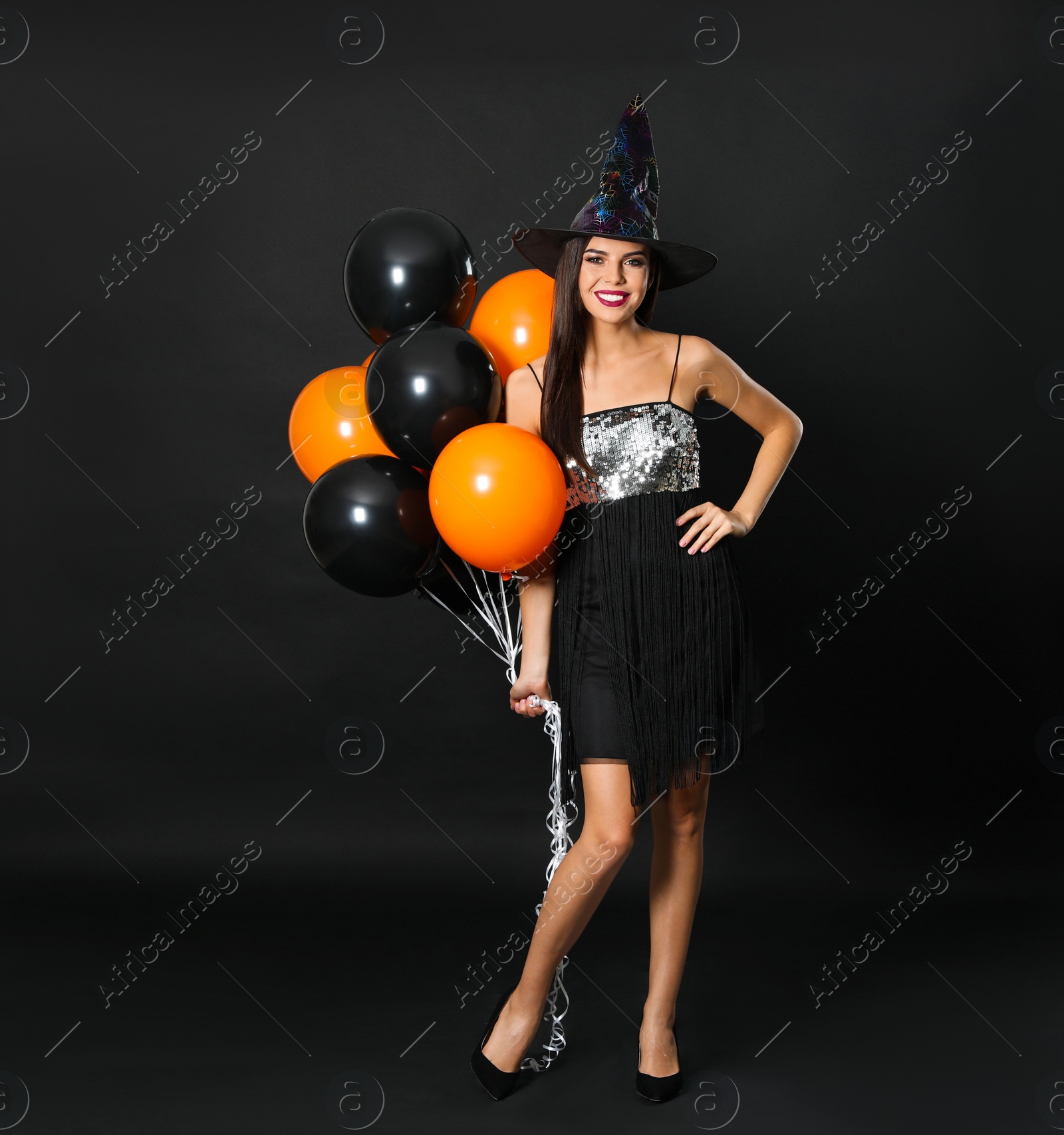 Photo of Beautiful woman wearing witch costume with balloons for Halloween party on black background