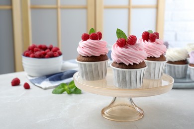 Photo of Delicious cupcakes with cream and raspberries on light grey marble table indoors. Space for text