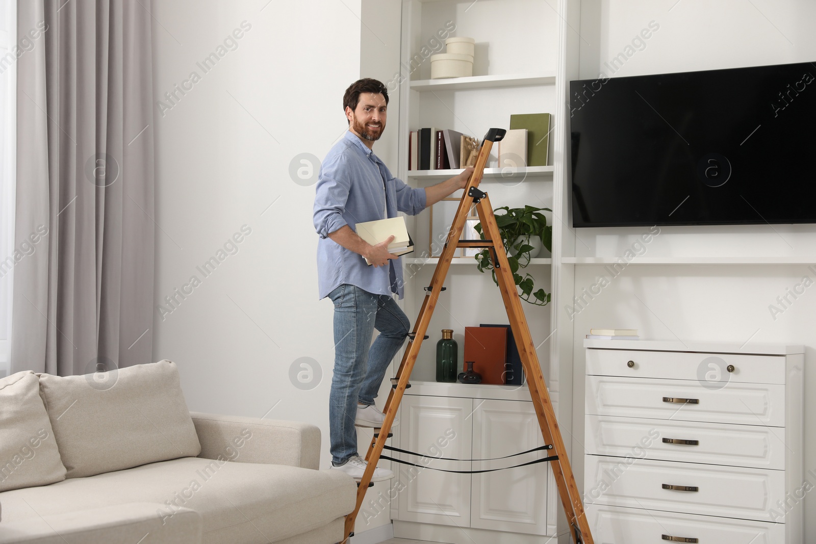 Photo of Man with books on wooden folding ladder at home