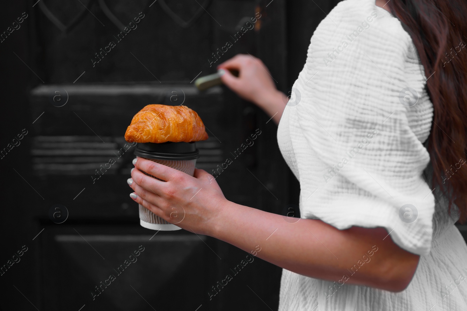 Photo of Woman with tasty croissant opening door, closeup view