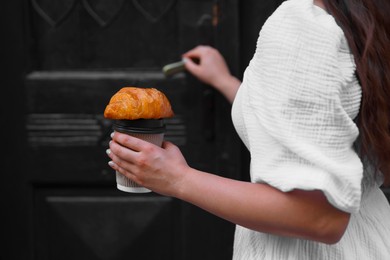 Woman with tasty croissant opening door, closeup view