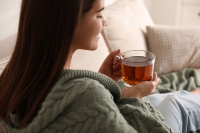 Photo of Woman covered with warm green plaid enjoying hot tea at home