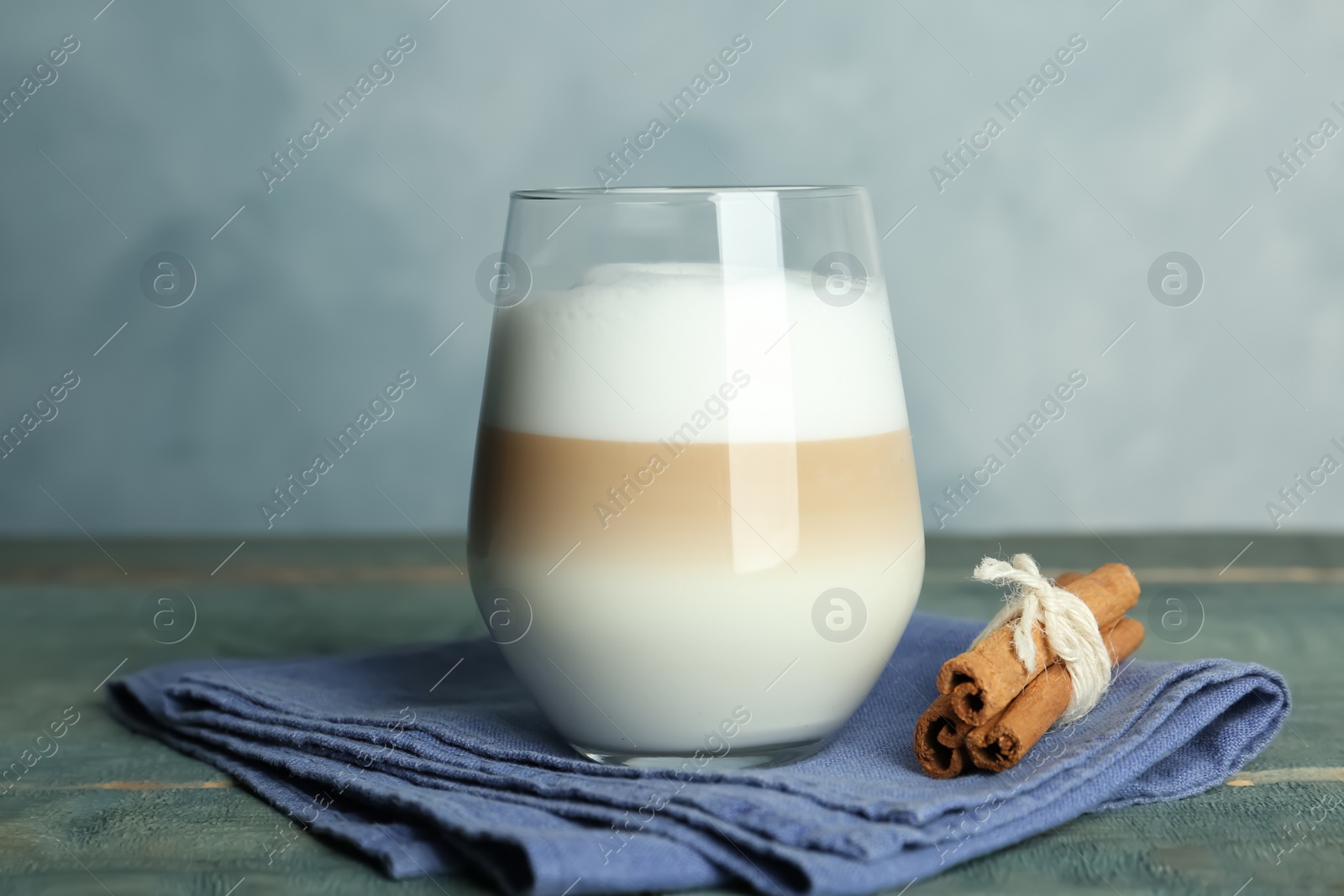 Photo of Delicious latte macchiato and cinnamon on wooden table against light blue background