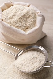 Photo of Sieve with quinoa flour near sack on wooden table