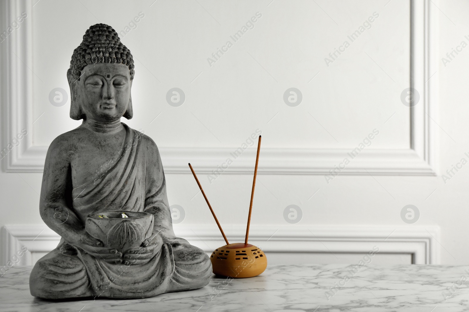 Photo of Buddha statue and incense sticks on white marble table. Space for text