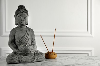 Photo of Buddha statue and incense sticks on white marble table. Space for text