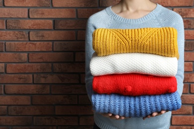 Woman holding pile of winter sweaters near brick wall, closeup view. Space for text