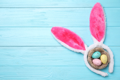 Headband with bunny ears, painted eggs and space for text on light blue wooden background, flat lay. Easter holiday