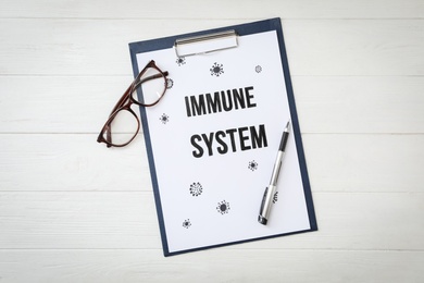 Photo of Clipboard with phrase Immune System, pen and glasses on white wooden table, flat lay