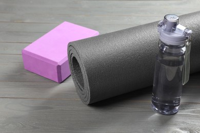 Photo of Exercise mat, yoga block and bottle of water on grey wooden floor