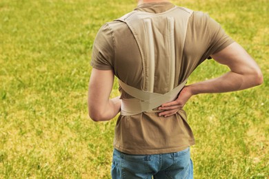 Photo of Closeup of man with orthopedic corset on green grass outdoors, back view
