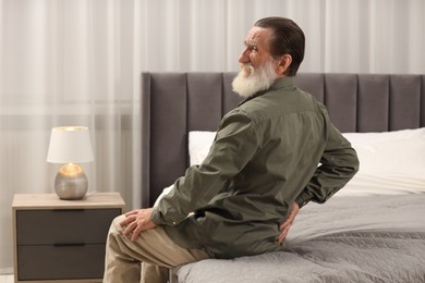 Senior man suffering from back pain on bed at home. Rheumatism symptom