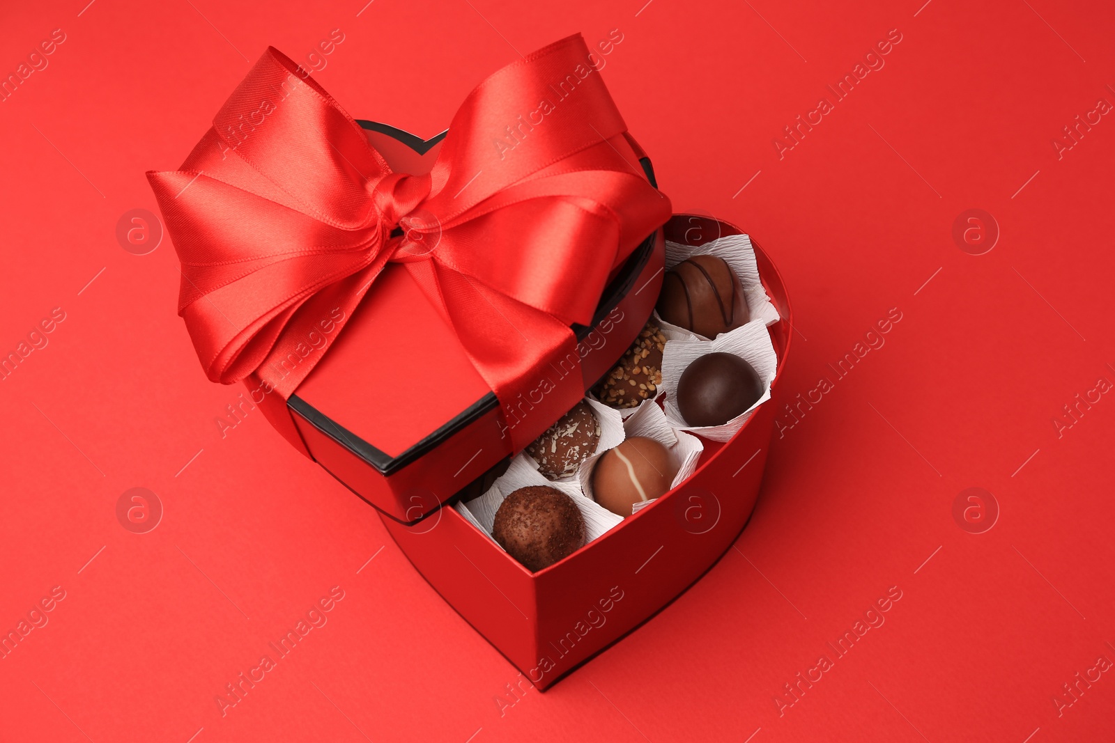 Photo of Heart shaped box with delicious chocolate candies on red table