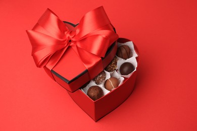 Photo of Heart shaped box with delicious chocolate candies on red table