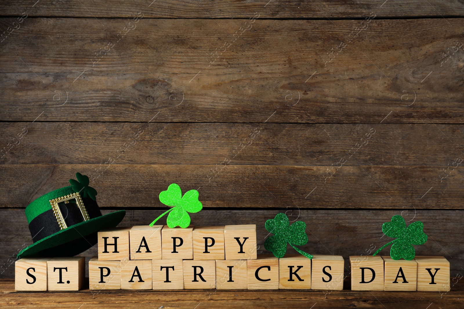 Photo of Wooden cubes with words HAPPY ST PATRICK'S DAY, green leprechaun hat and clover leaves on table