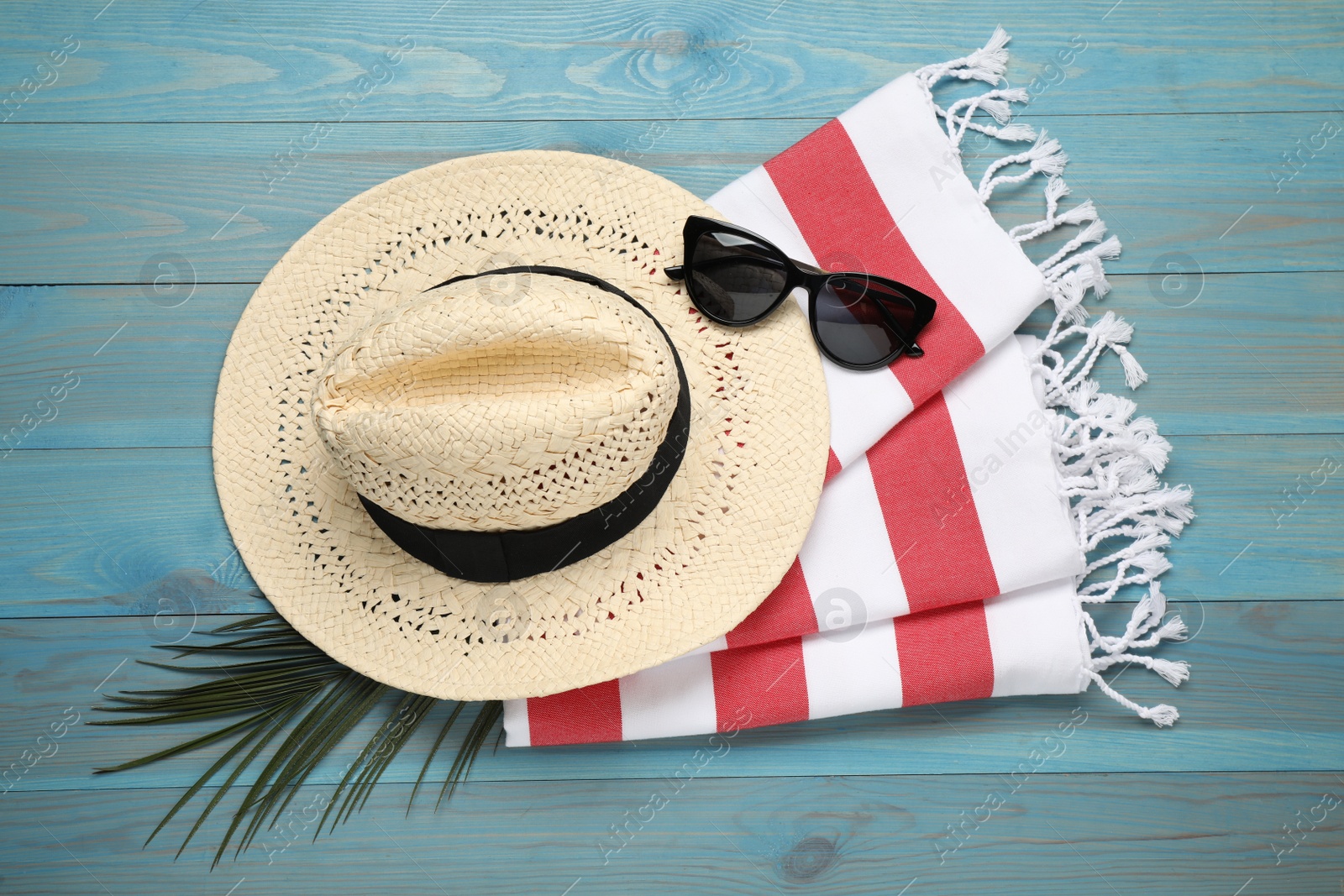 Photo of Beach towel, sunglasses and straw hat on light blue wooden background, flat lay
