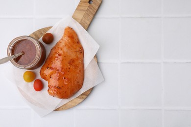 Photo of Fresh marinade and raw chicken fillets on white tiled table, top view. Space for text